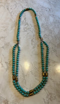 This is a long turquoise bead necklace featuring interspersed gold-tone oblong beads.