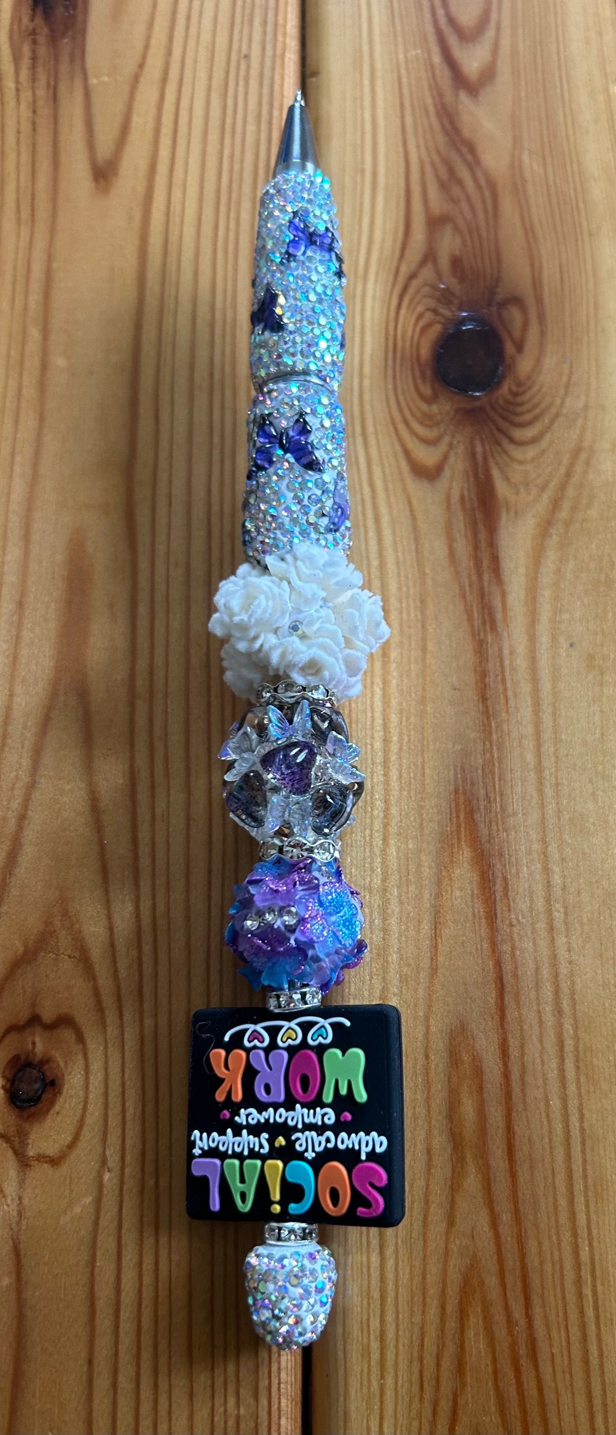 This customized beadable pen features a "Social Work" topper and is decorated with purple butterflies over a rhinestoned barrel.It is crafted with a combination of rhinestone and acrylic beads, making it a functional luxury writing instrument.