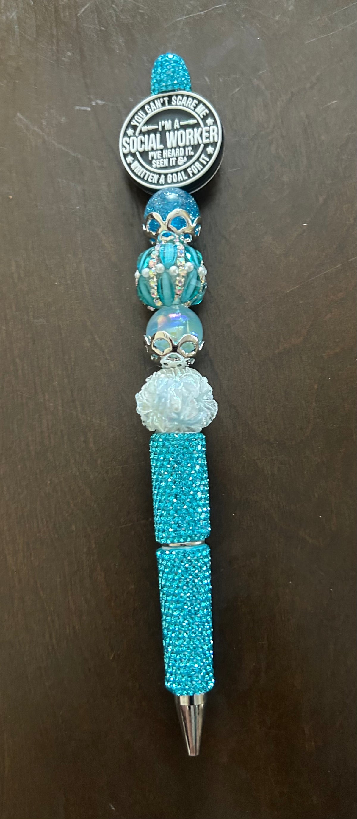 This custom-made, turquoise beaded pen features a social worker slogan and sparkling rhinestone accents.It is designed with a light blue barrel and a beaded top, similar to handmade rhinestone pens sold online.