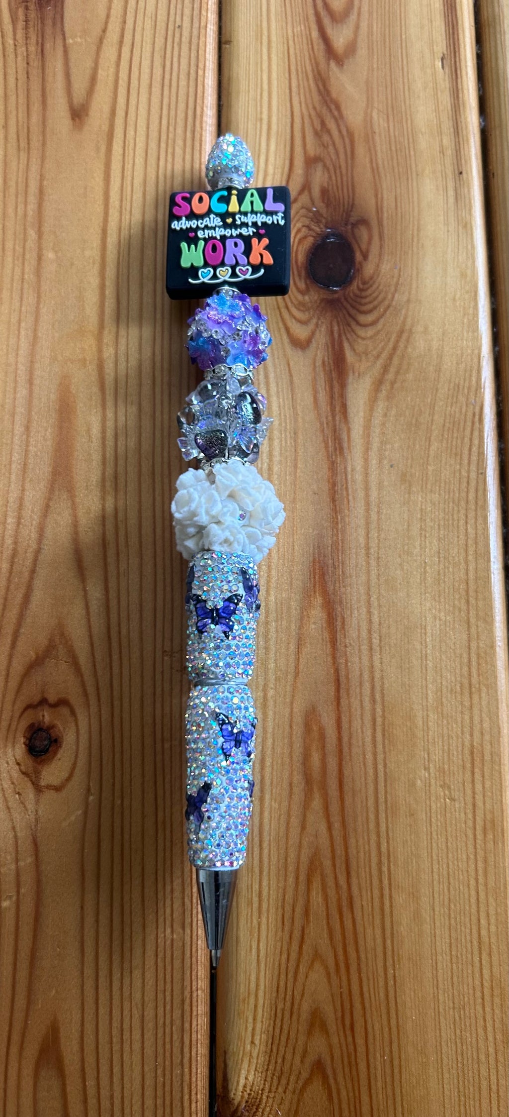This customized beadable pen features a "Social Work" topper and is decorated with purple butterflies over a rhinestoned barrel.It is crafted with a combination of rhinestone and acrylic beads, making it a functional luxury writing instrument.