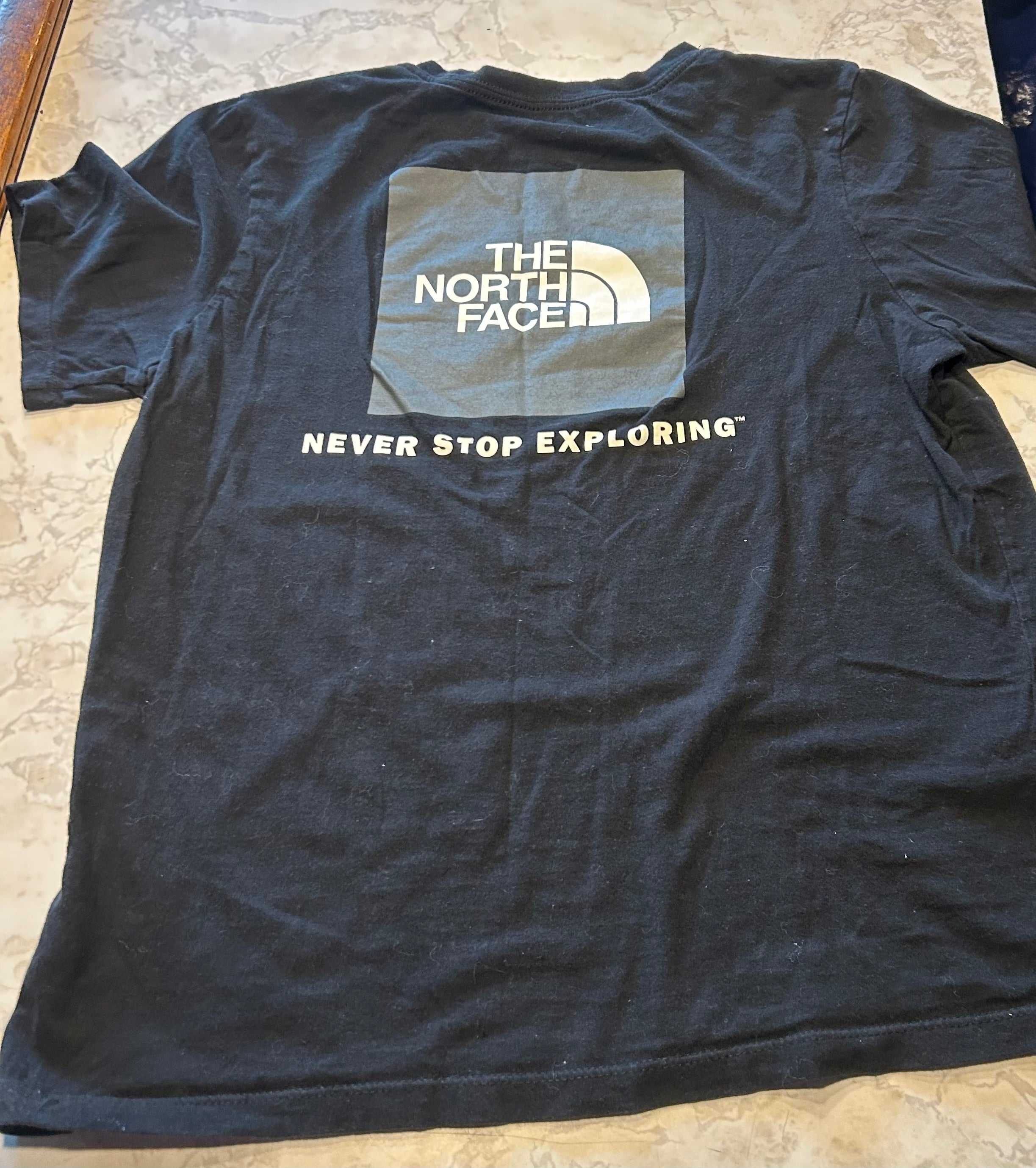 This black is medium North Face "Never Stop Exploring" crew neck t-shirt features a large graphic logo box on the back.