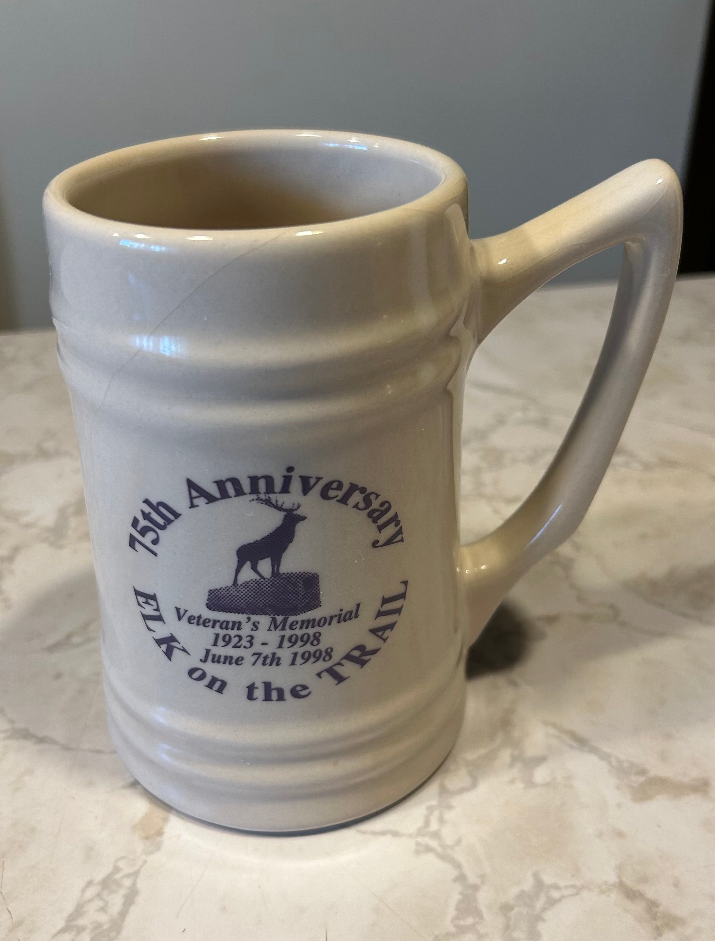 This is a white ceramic beer mug commemorating the 75th Anniversary of an Elk Lodge Veterans Memorial in 1998.