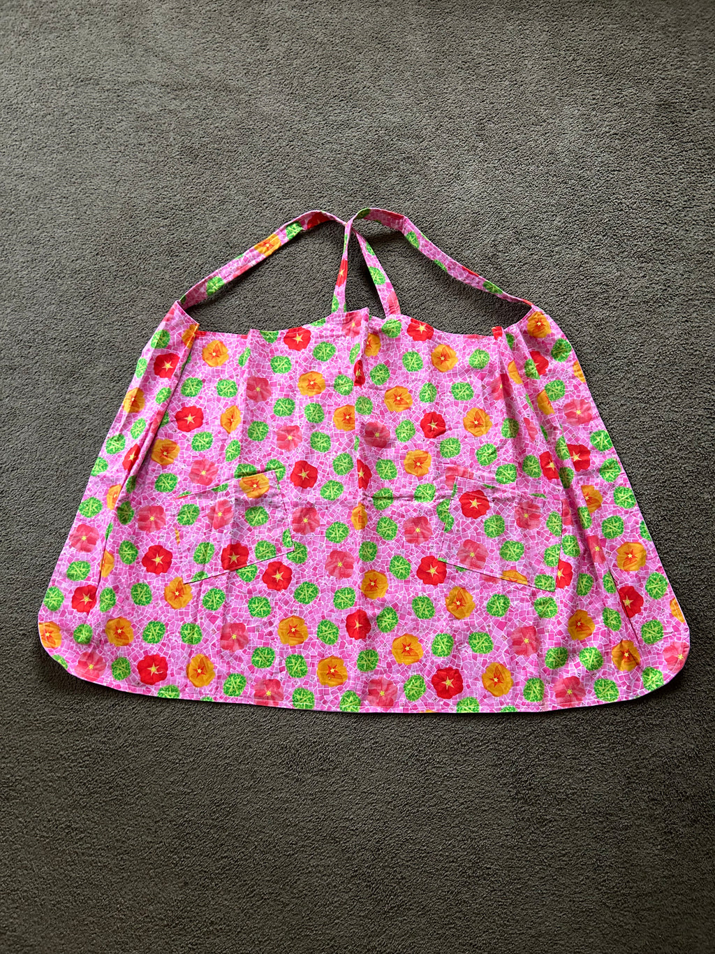 This floral patterned apron features two front pockets and a pink base color.