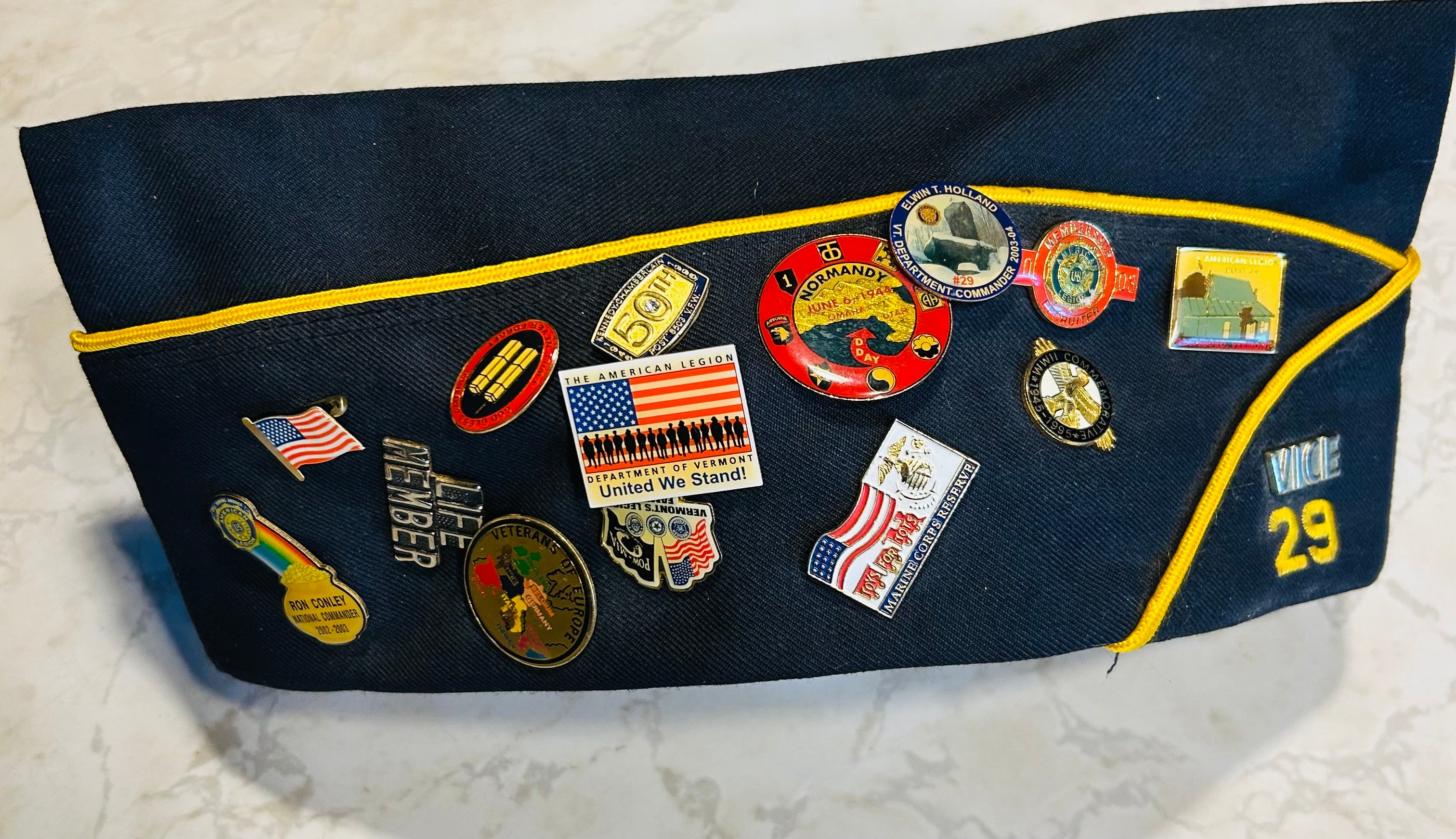 This is a blue American Legion veteran overseas cap adorned with various commemorative pins.